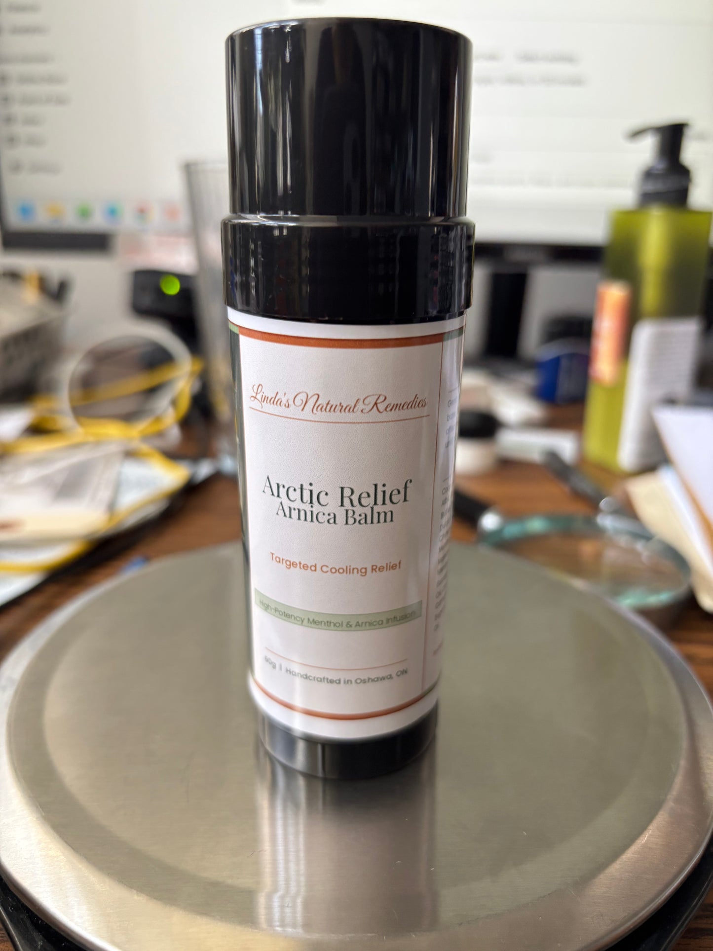 Lifestyle photo of Arctic Relief Arnica Balm by Linda's Natural Remedies, showing the 60g eco-friendly push-up tube. The artisan label features a copper and sage green design for a natural, high-end look.