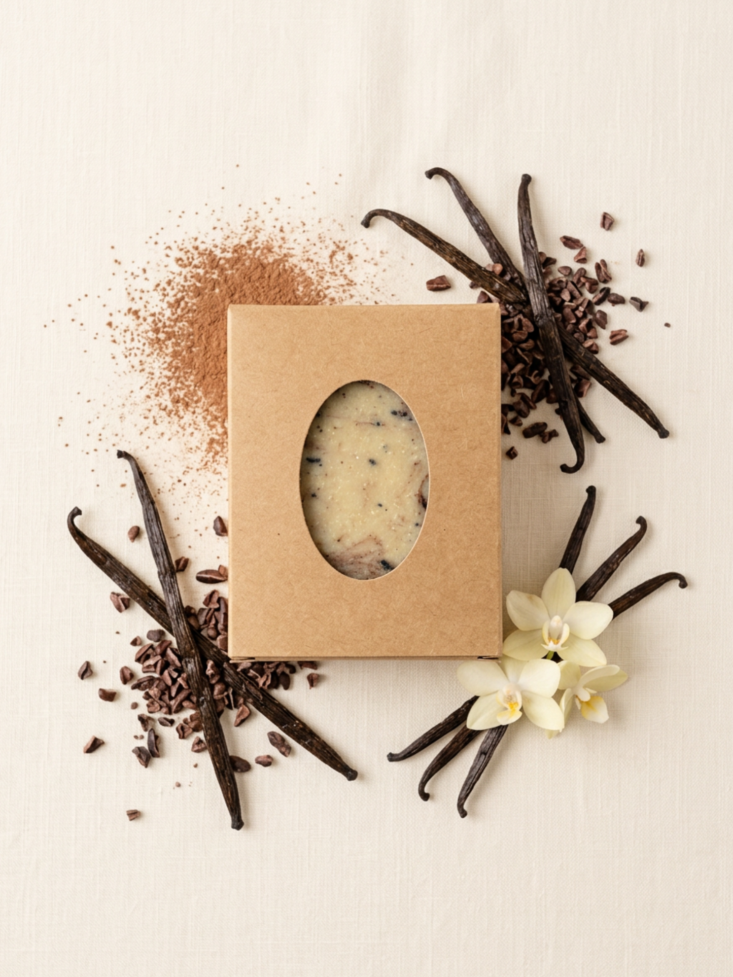 Bar of soap in a cardboard box surrounded by vanilla beans and a flower on a light background