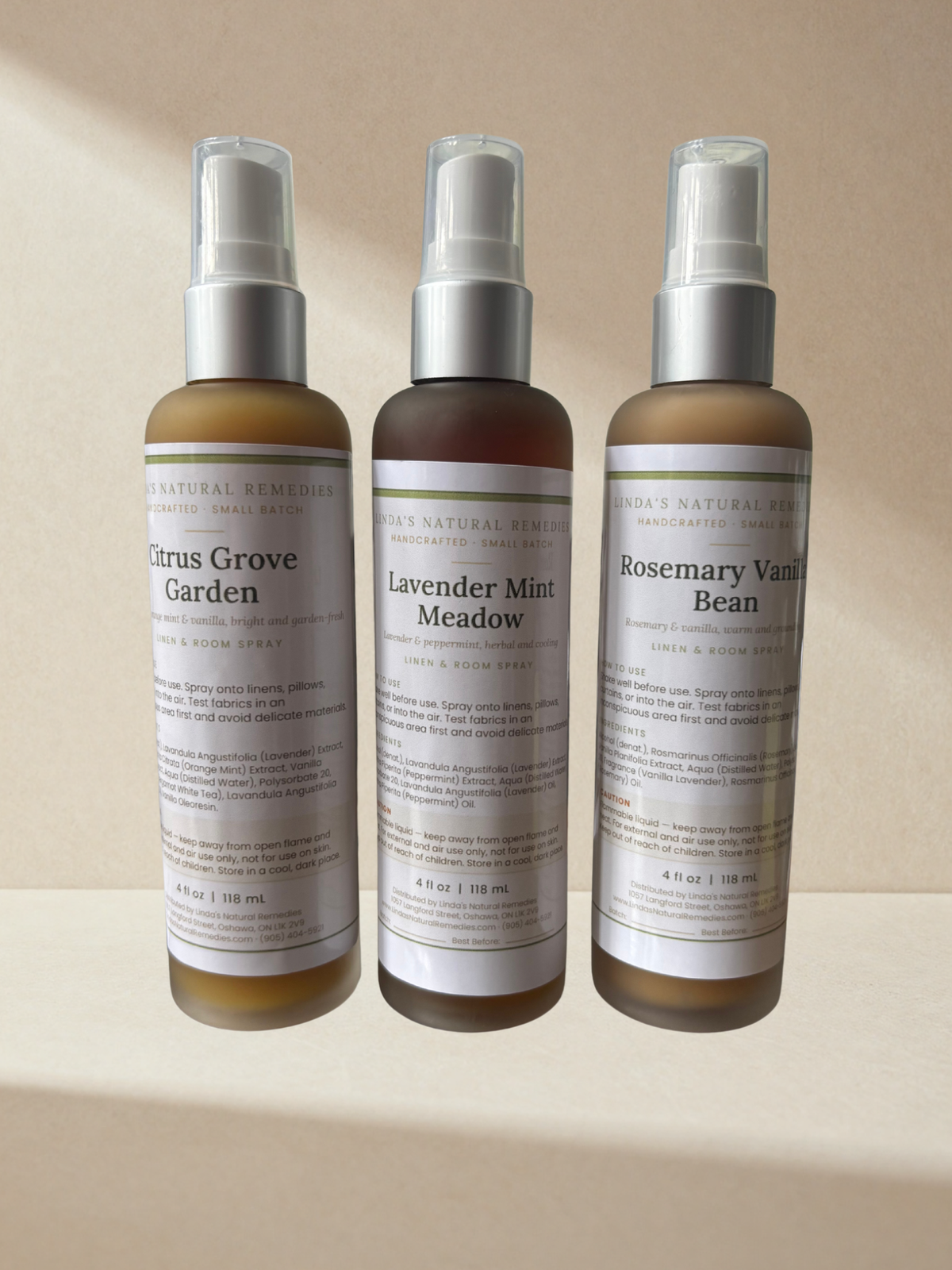 Three amber glass spray bottles of Linda's Natural Remedies linen and room sprays with silver pump tops, standing side by side on a warm beige surface — Citrus Grove Garden, Lavender Mint Meadow, and Rosemary Vanilla Bean, each 4 oz / 118 ml.