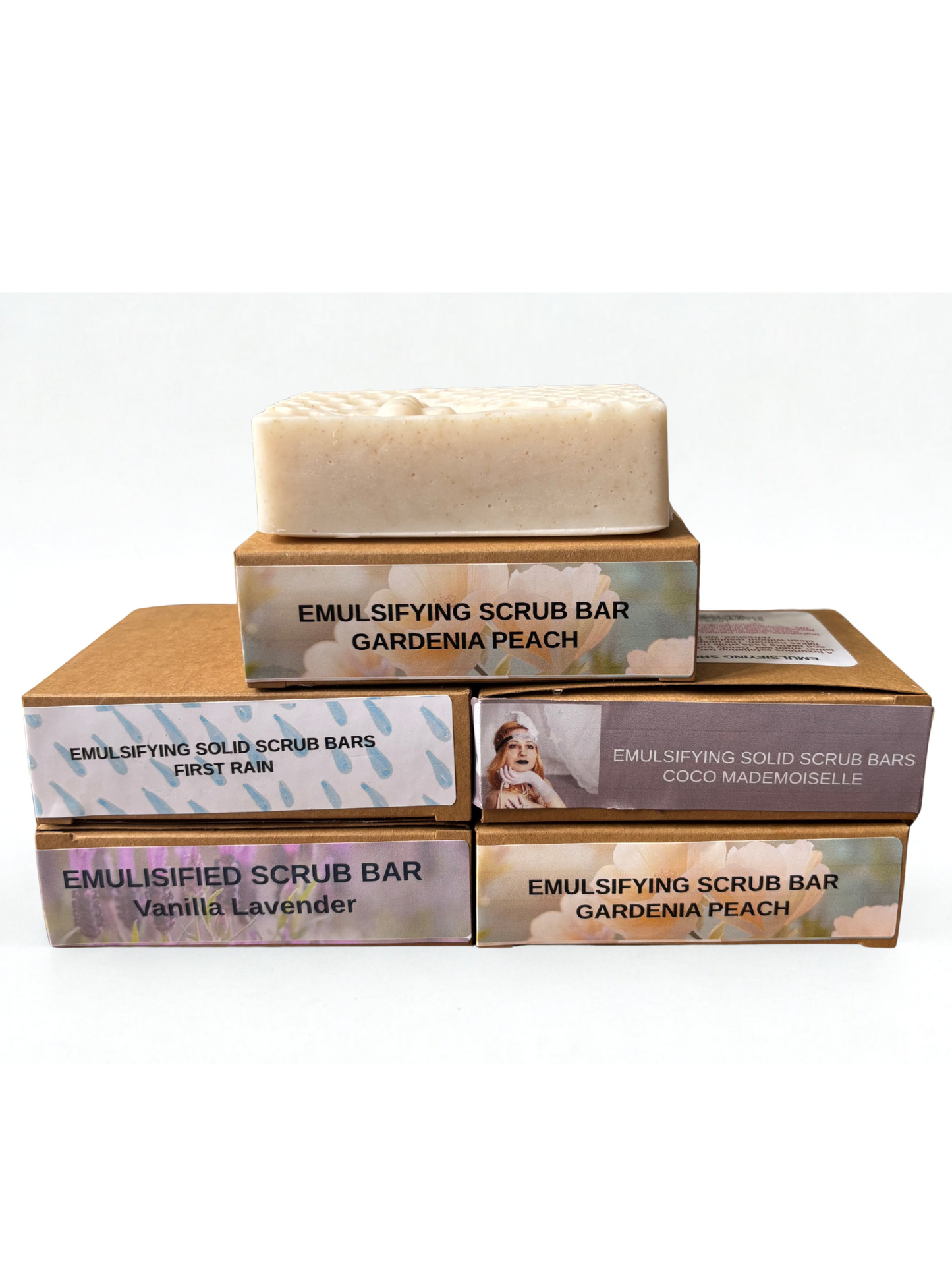 Stack of emulsifying scrub bar boxes with a gardenia peach bar on top against a white background