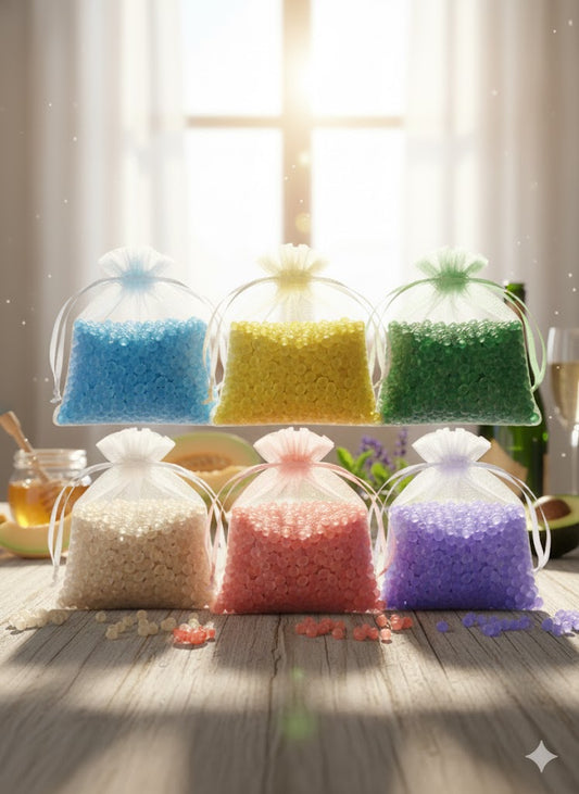 A complete collection of six handmade aroma bead sachets in white organza bags, featuring vibrant shades of blue, yellow, green, champagne, coral, and purple, displayed on a rustic wooden table in natural sunlight