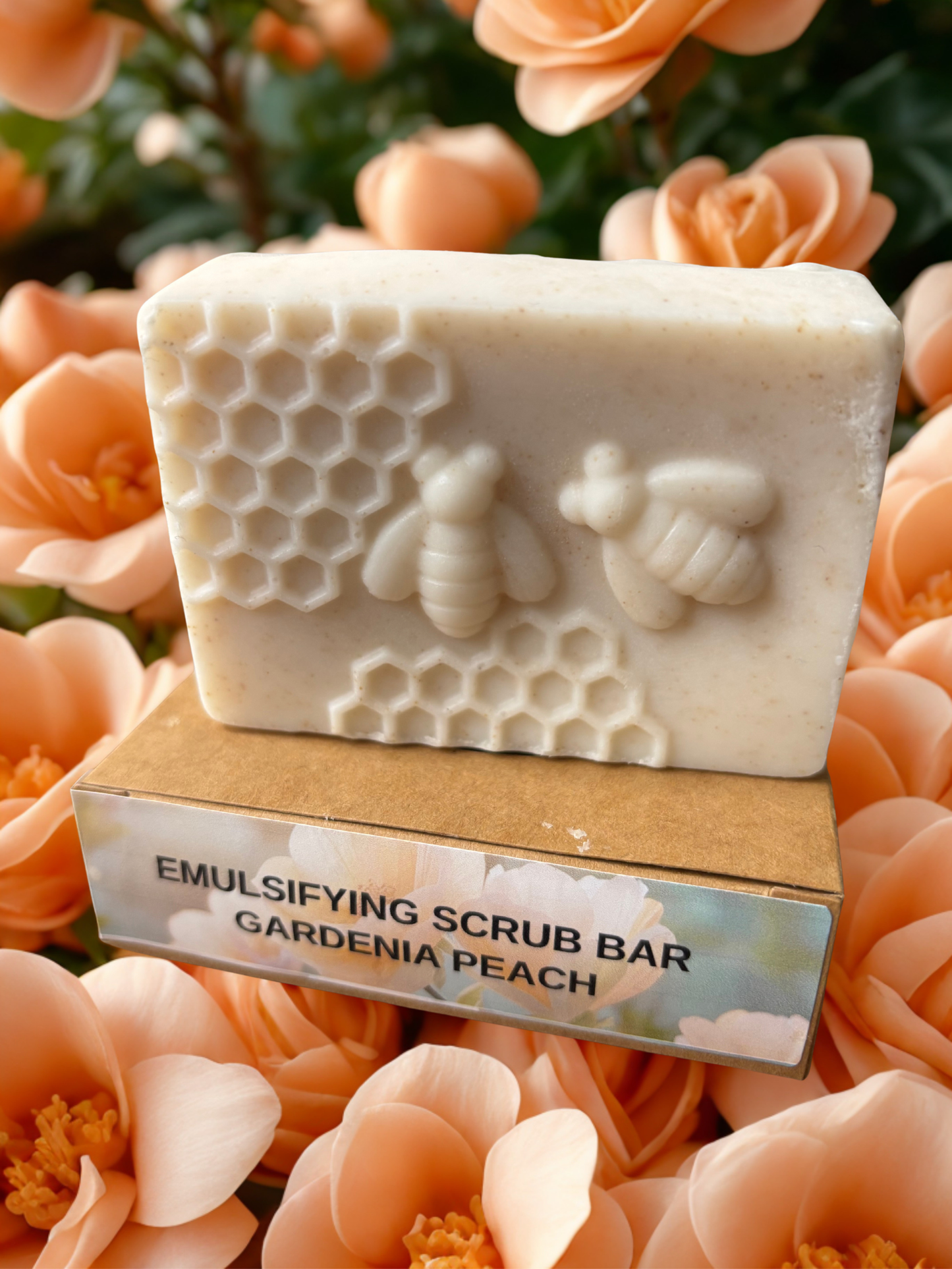 Emulsifying scrub bar with honeycomb and bee design on a wooden block, surrounded by gardenia peach flowers.