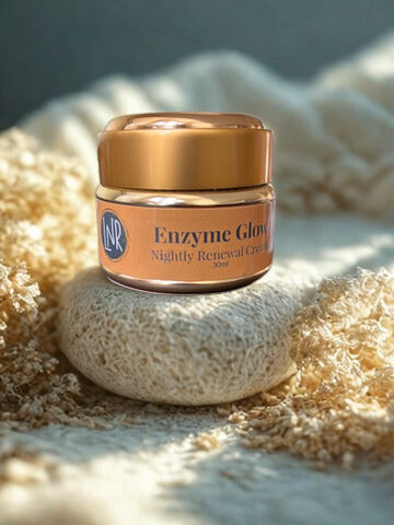 A gold jar of Linda’s Natural Remedies Enzyme Glow Nightly Renewal Cream resting on a natural loofah sponge, surrounded by soft, cream-colored botanicals in warm sunlight.