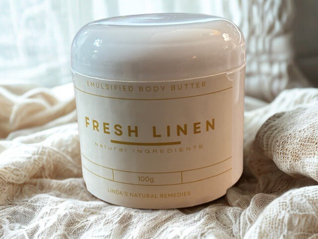 Jar of emulsified body butter labeled 'Fresh Linen' on a soft fabric background