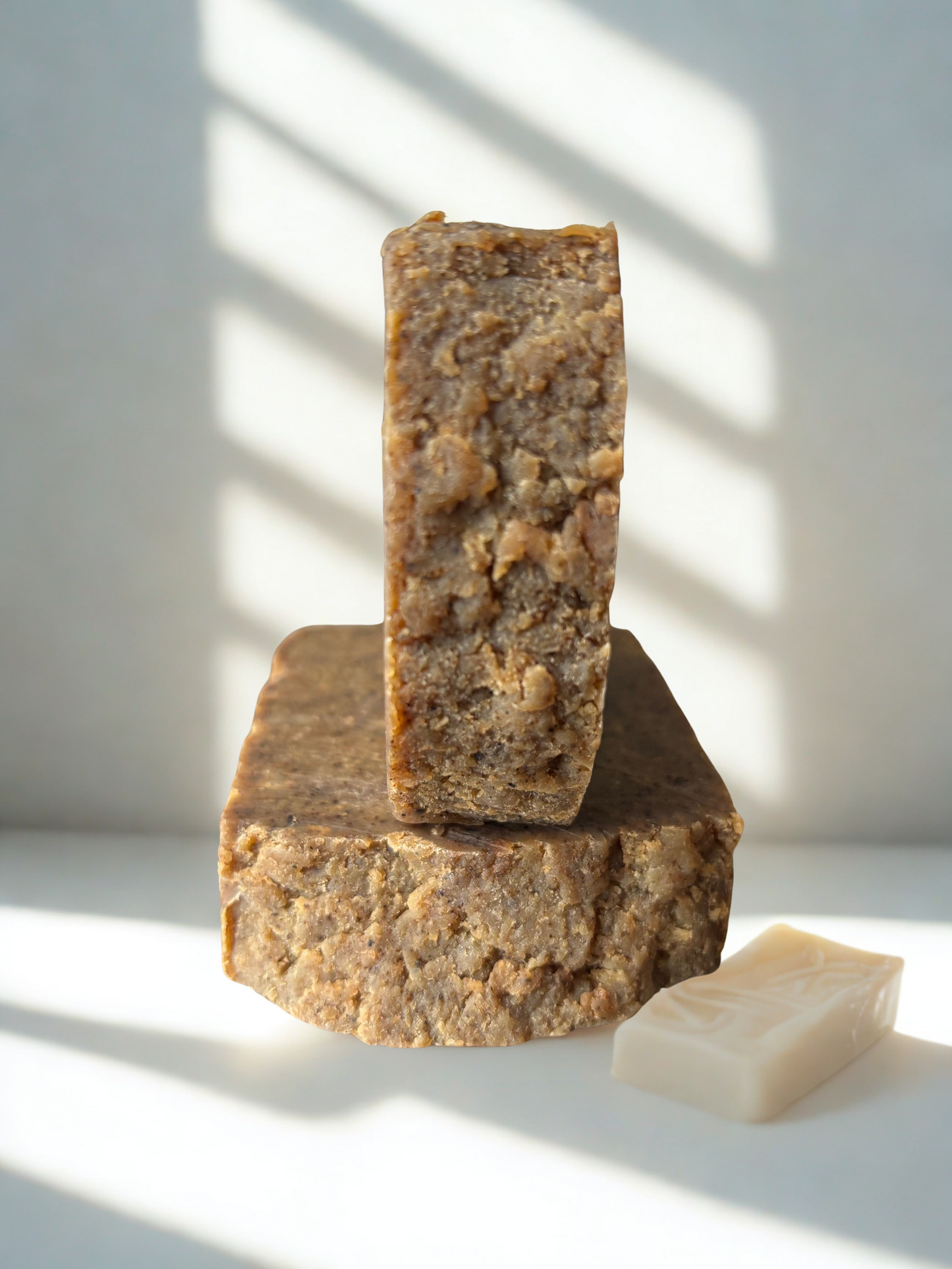 Three bars of brown soap stacked on a white surface with shadows cast by sunlight.