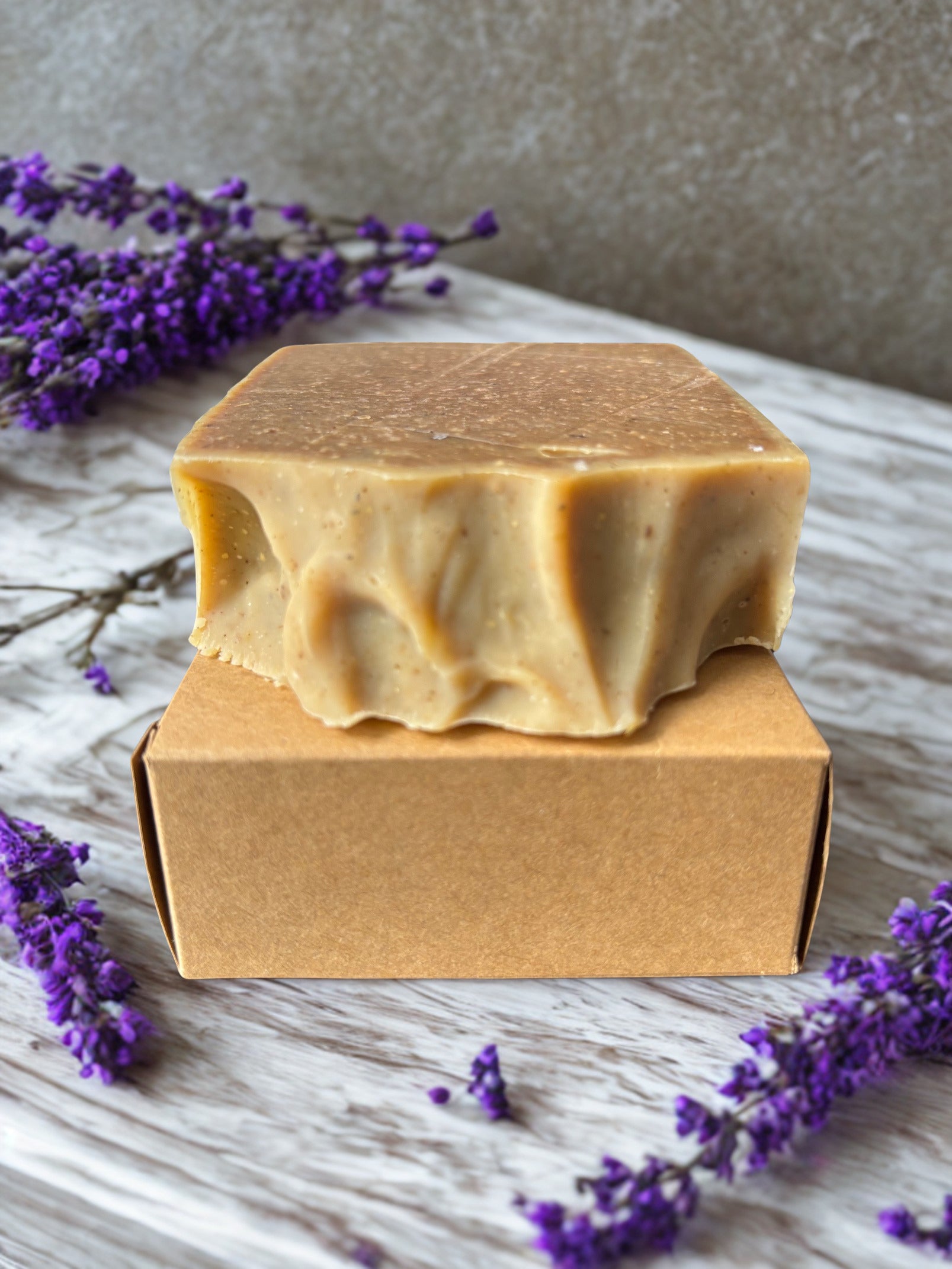 Bar of soap on a brown box with lavender flowers around on a wooden surface