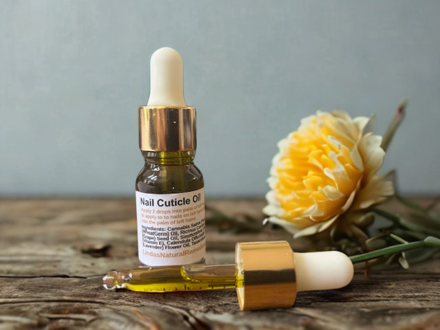 "Linda's Natural Remedies Nail Cuticle Oil in a clear glass dropper bottle, showing the beautiful natural blue-green tint from infused blue tansy and lavender oils."