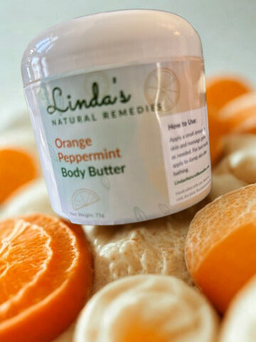 A jar of Linda's Natural Remedies Orange Peppermint Body Butter surrounded by fresh orange slices and peppermint leaves.