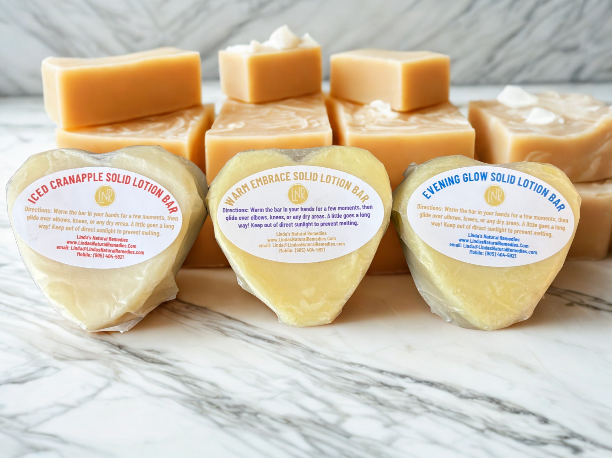 A collection of three Luxe Heart Lotion Bars by Linda's Natural Remedies, hand-wrapped in wax paper and ready for shipping. Scents: Warm Embrace, Evening Glow, and Iced Cranapple.