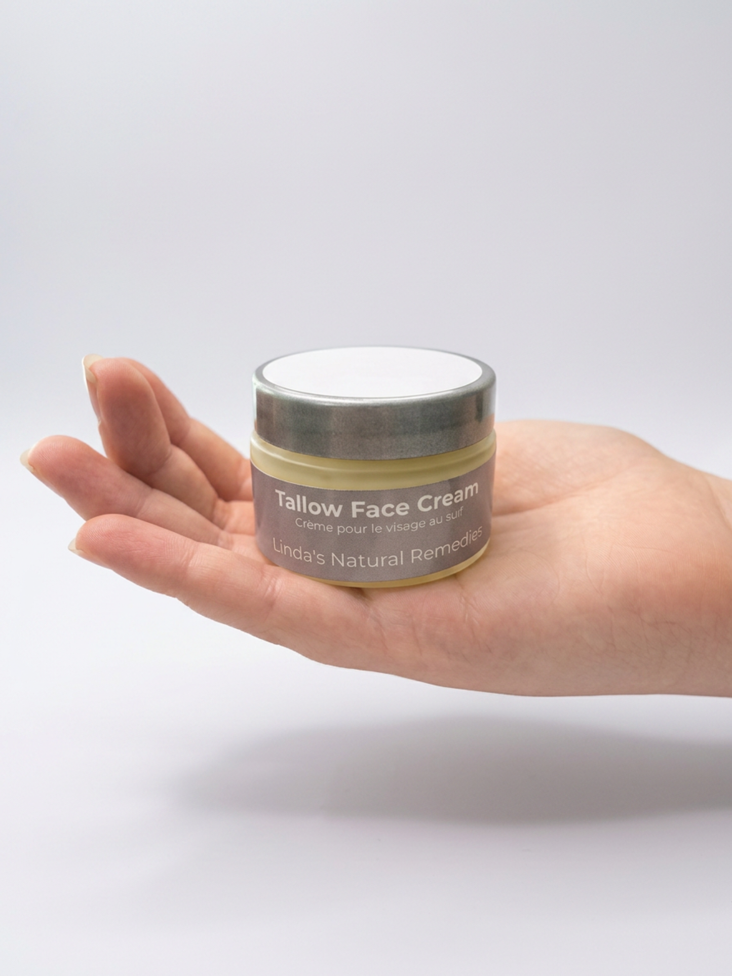 Hand holding a jar of tallow face cream against a plain background