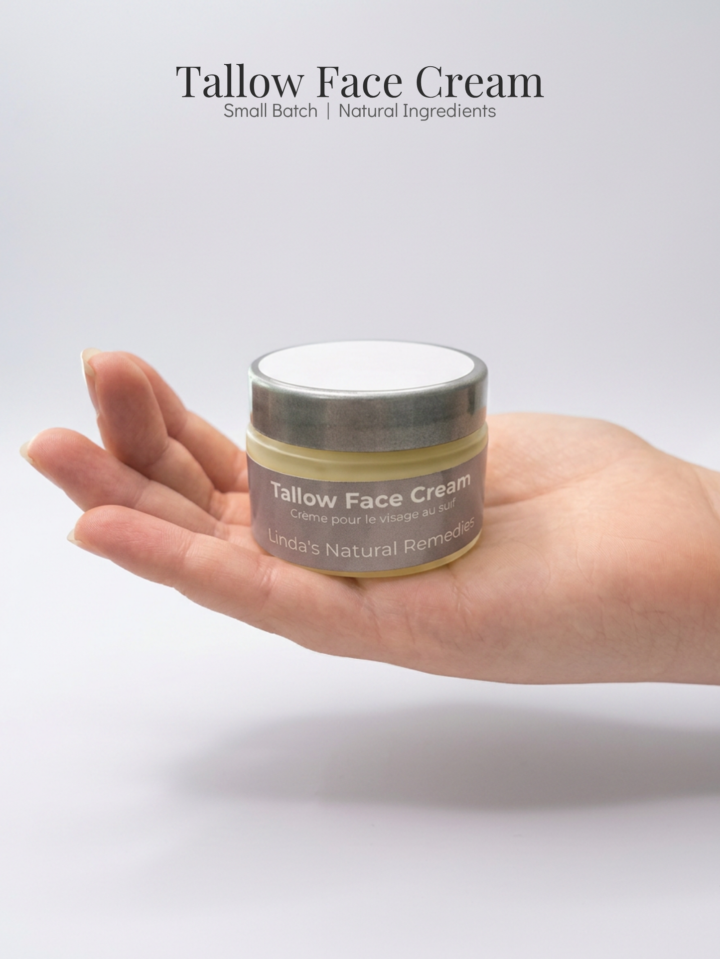 Hand holding a jar of tallow face cream with a plain background