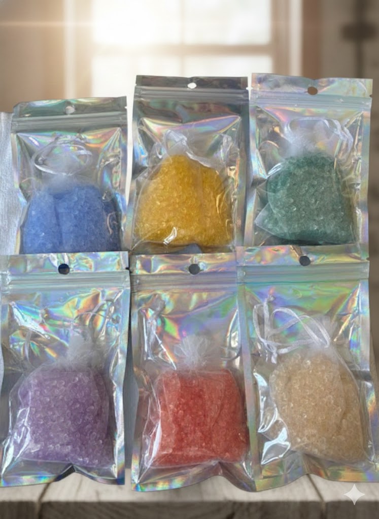 A complete collection of six handmade aroma bead sachets in white organza bags, featuring vibrant shades of blue, yellow, green, champagne, coral, and purple, displayed on a rustic wooden table in natural sunlight