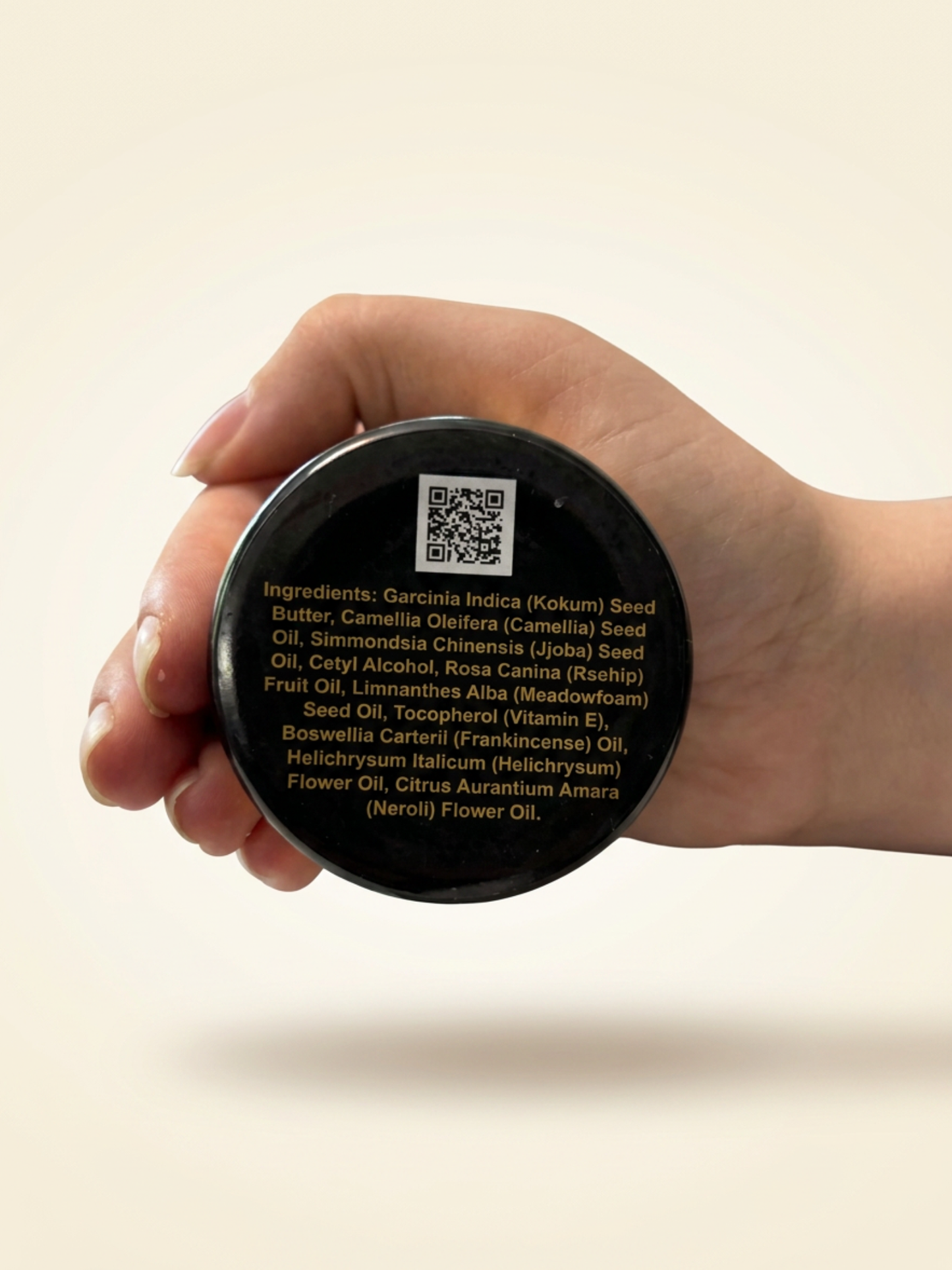 Hand holding a container with a QR code and ingredients text on a beige background